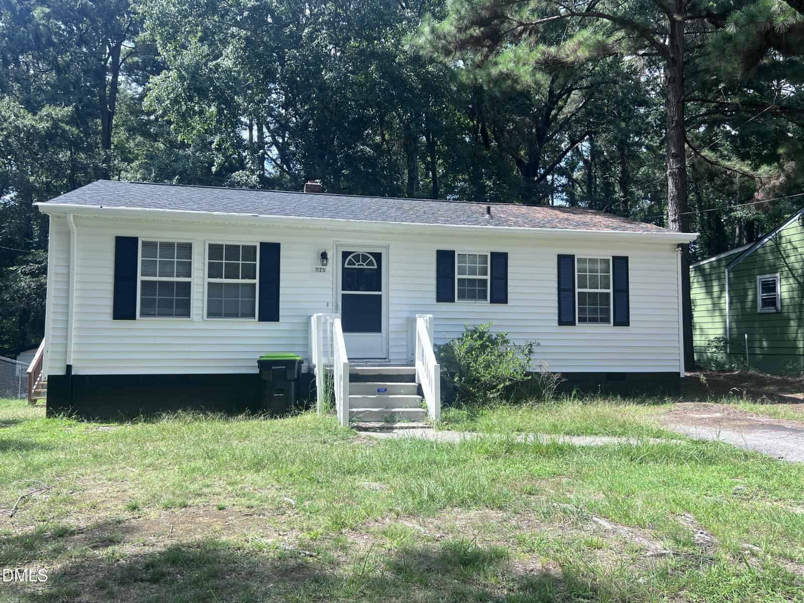Single-story white house with black shutters, a small front porch, two steps leading to the door, and surrounded by trees and grass. Located at 125 Booth Avenue in Henderson, this charming home features a green trash bin near the front steps.
