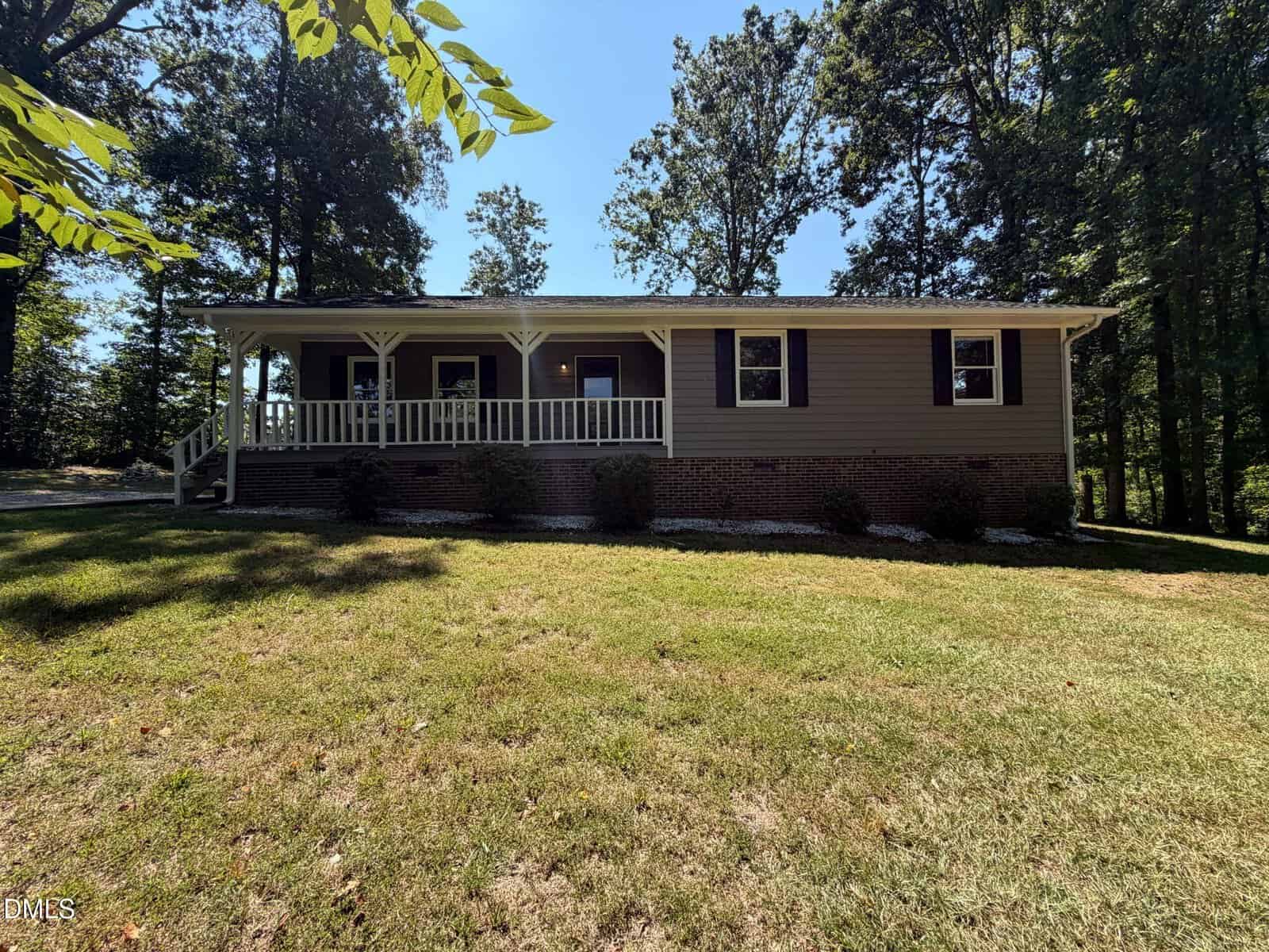 A single-story house with a covered front porch, brick foundation, and tan siding sits at 130 Rolling Acres Road in Youngsville, surrounded by trees and grass on a sunny day.