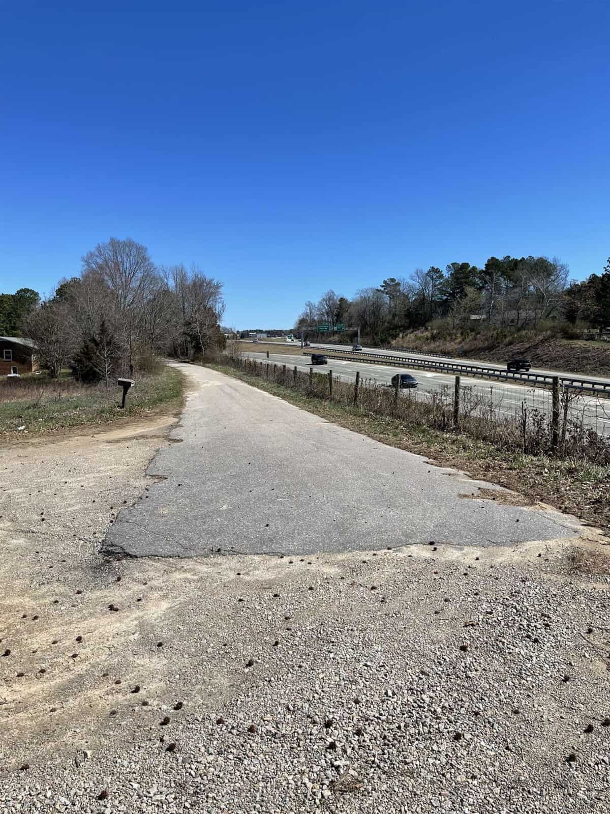 A paved pathway runs alongside a highway under a clear blue sky, with traffic visible on the road and sparse vegetation on either side.