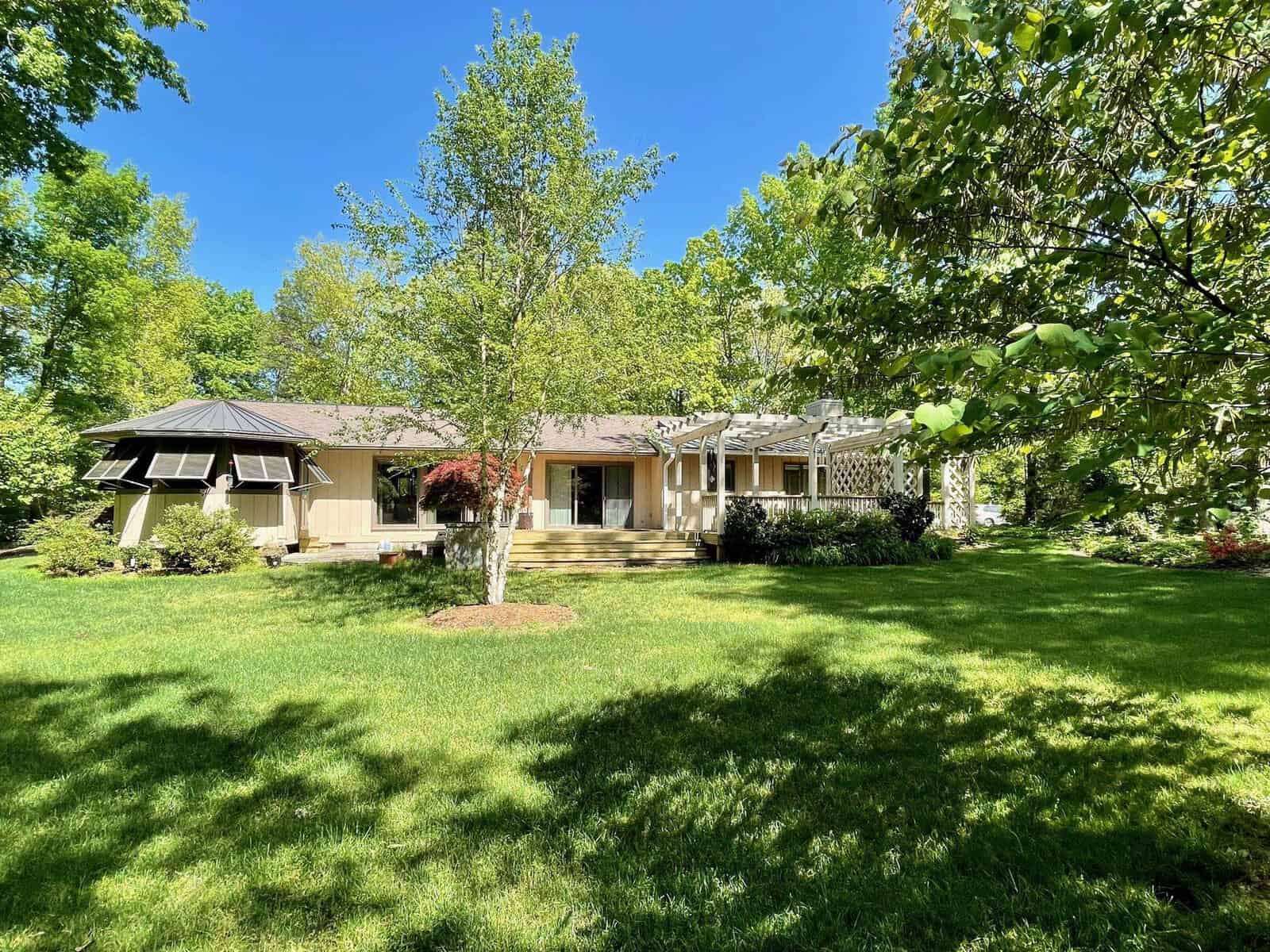 Single-story house with a well-maintained lawn and surrounding trees on a sunny day.
