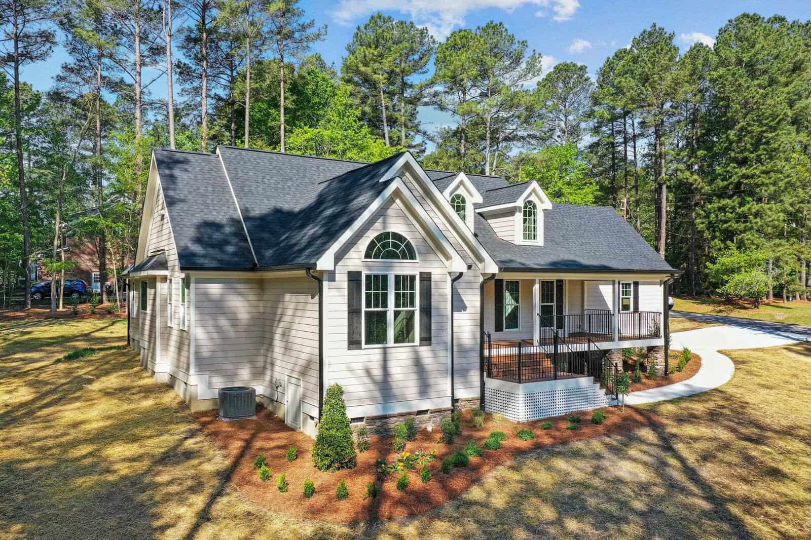 A single-family home with a gabled roof and a mix of siding and shingle exterior materials, surrounded by a freshly landscaped yard with young trees and shrubs, under a clear blue sky.