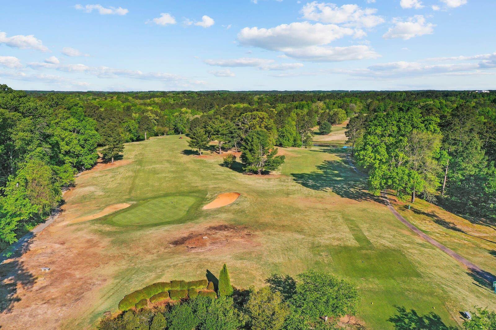 Aerial view of a golf course with manicured greens, sand traps, and surrounding woodland.