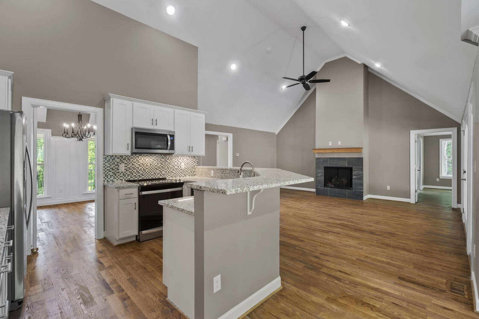 A spacious kitchen with white cabinetry and stainless steel appliances, featuring a central island with a granite countertop, adjacent to an open-plan living area with a fireplace and hardwood floors.