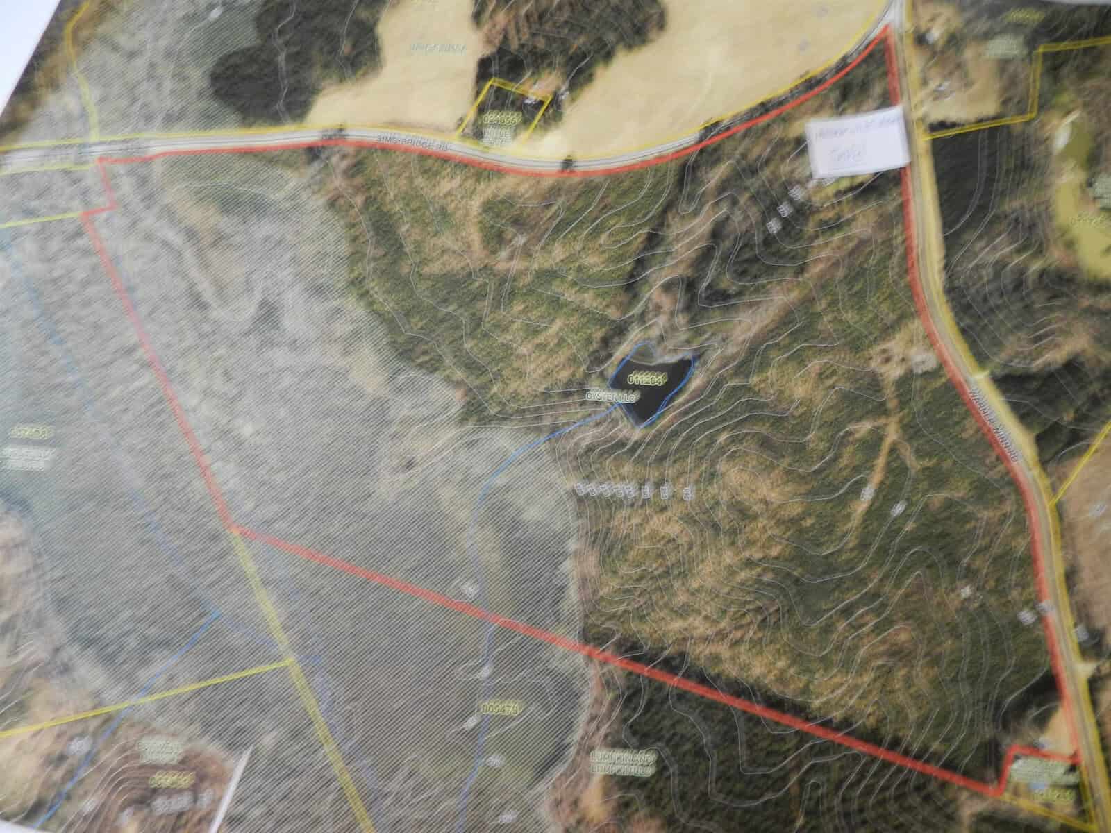 A blurred image of a topographic map that includes various elevations marked by contour lines, a body of water, and some labeled areas. Roads and paths are also visible, with some sections outlined in red and yellow.