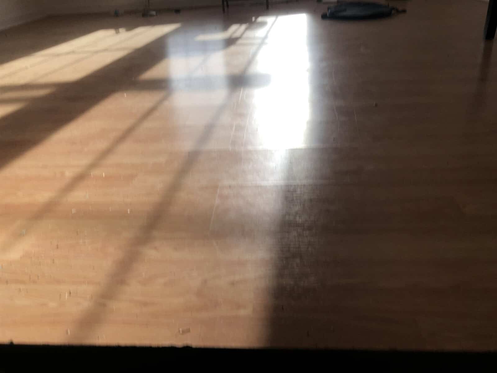 Sunlight casting shadows across a polished wooden floor in an empty room.