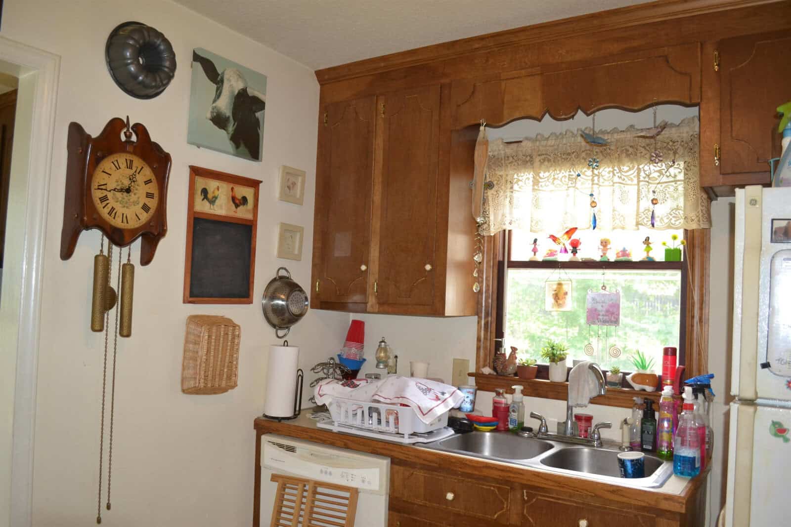 A homely kitchen with wooden cabinets, a clock on the wall, and various household items and cleaning products on the countertop.