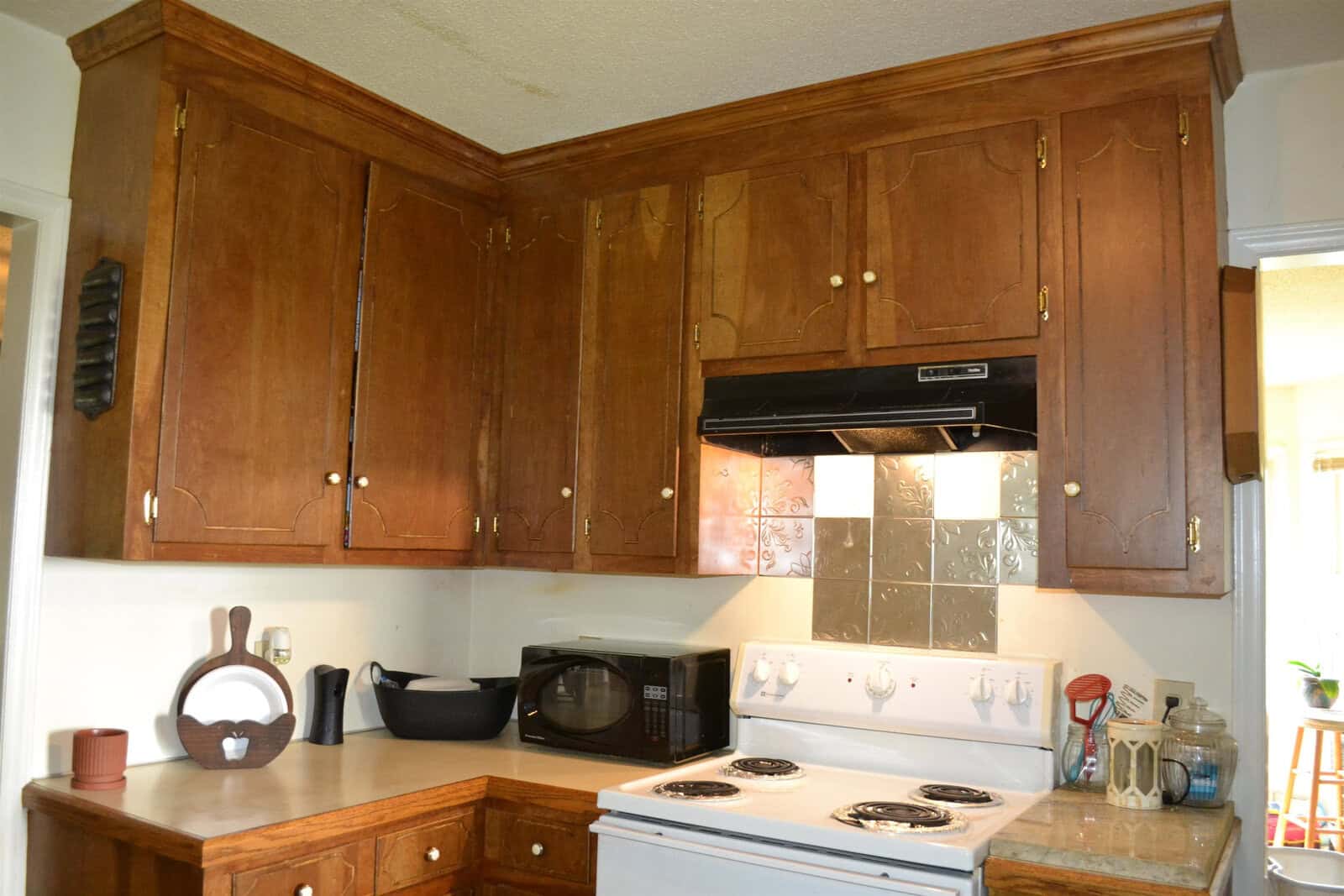 A kitchen interior featuring wooden cabinets, a white stove, a microwave, and various kitchen utensils and appliances on the countertop.