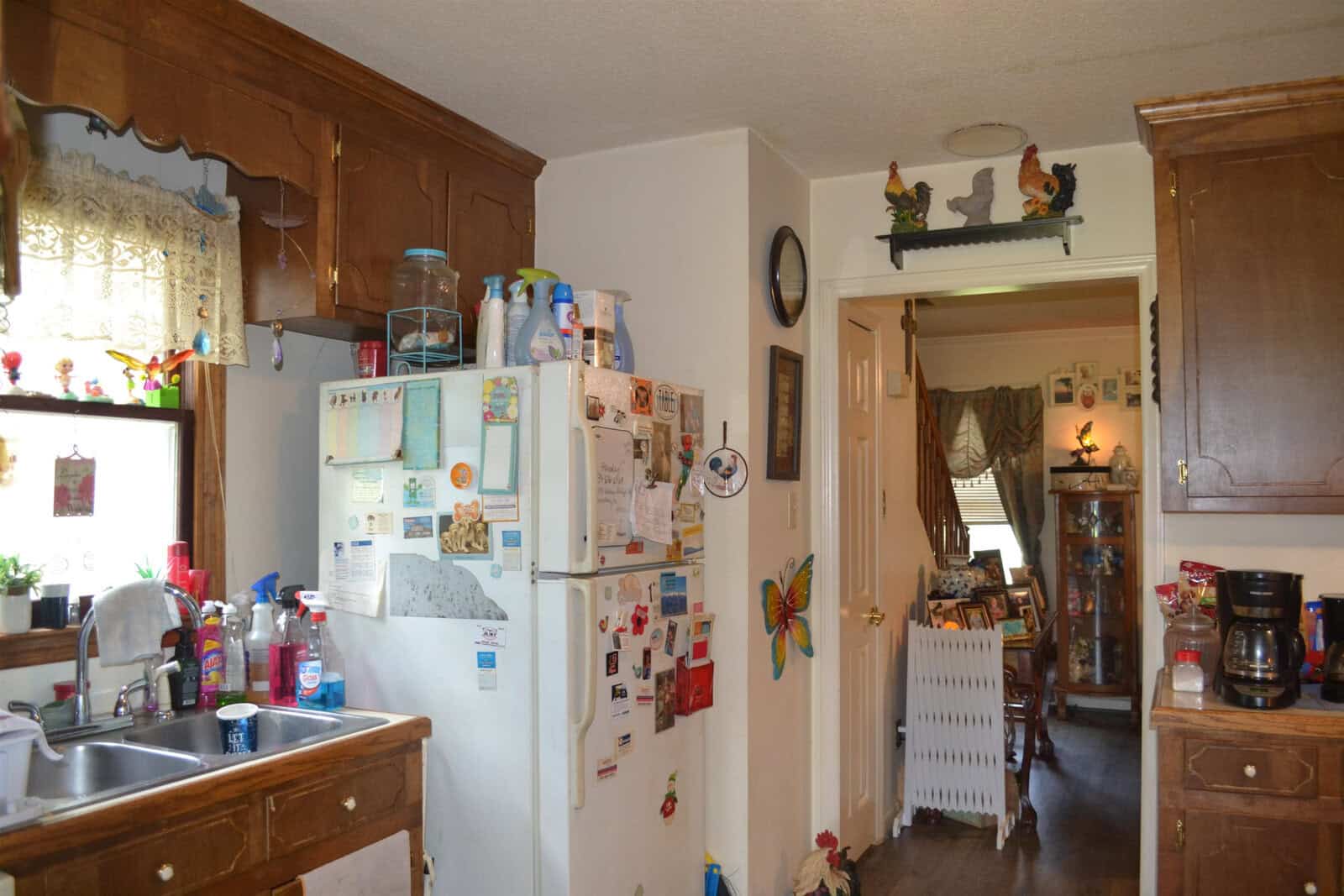 A cluttered kitchen with a white refrigerator covered in magnets and notices, a sink with blue sponges, and various items scattered on the countertops.