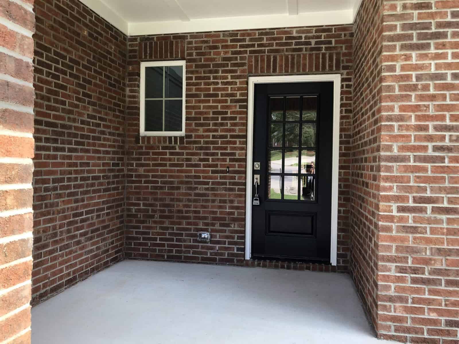 A residential entryway featuring a black front door and surrounding brick walls.