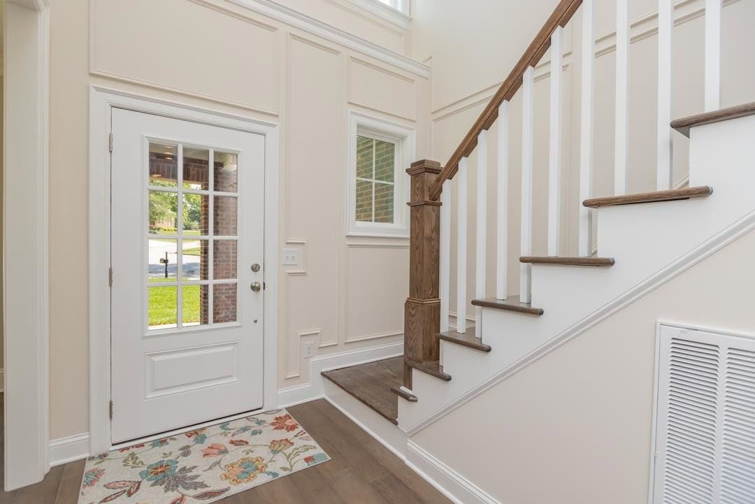 An entryway of a home featuring a white front door with sidelight windows, a wooden staircase with white balusters, and a floral area rug on hardwood flooring.
