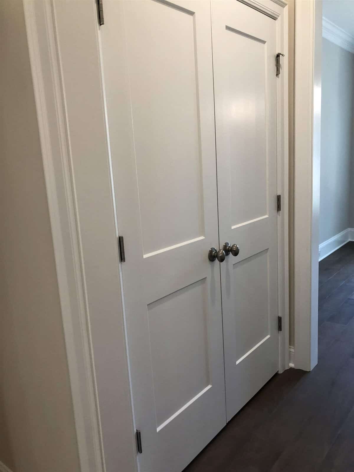A pair of white double doors with silver handles set in a wall within an interior space.