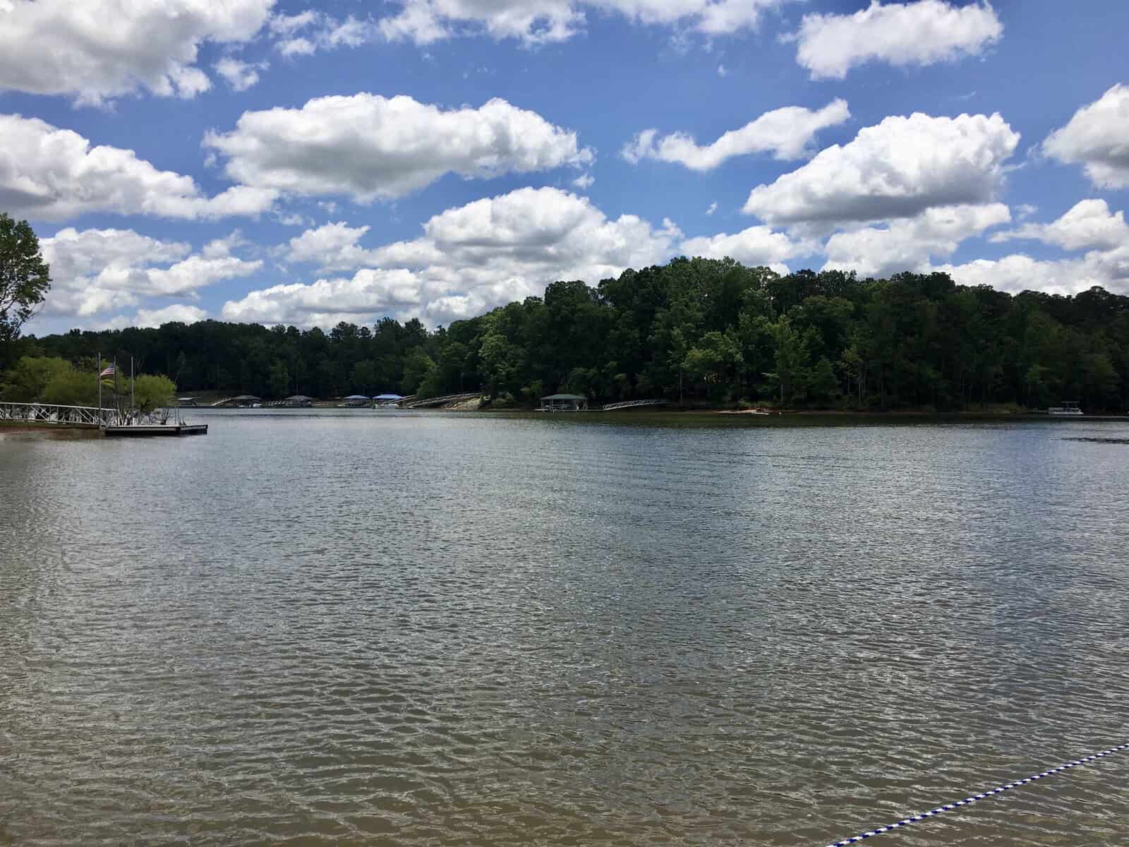 A serene lake surrounded by wooded areas under a cloudy sky, with boat docks visible along the shoreline.