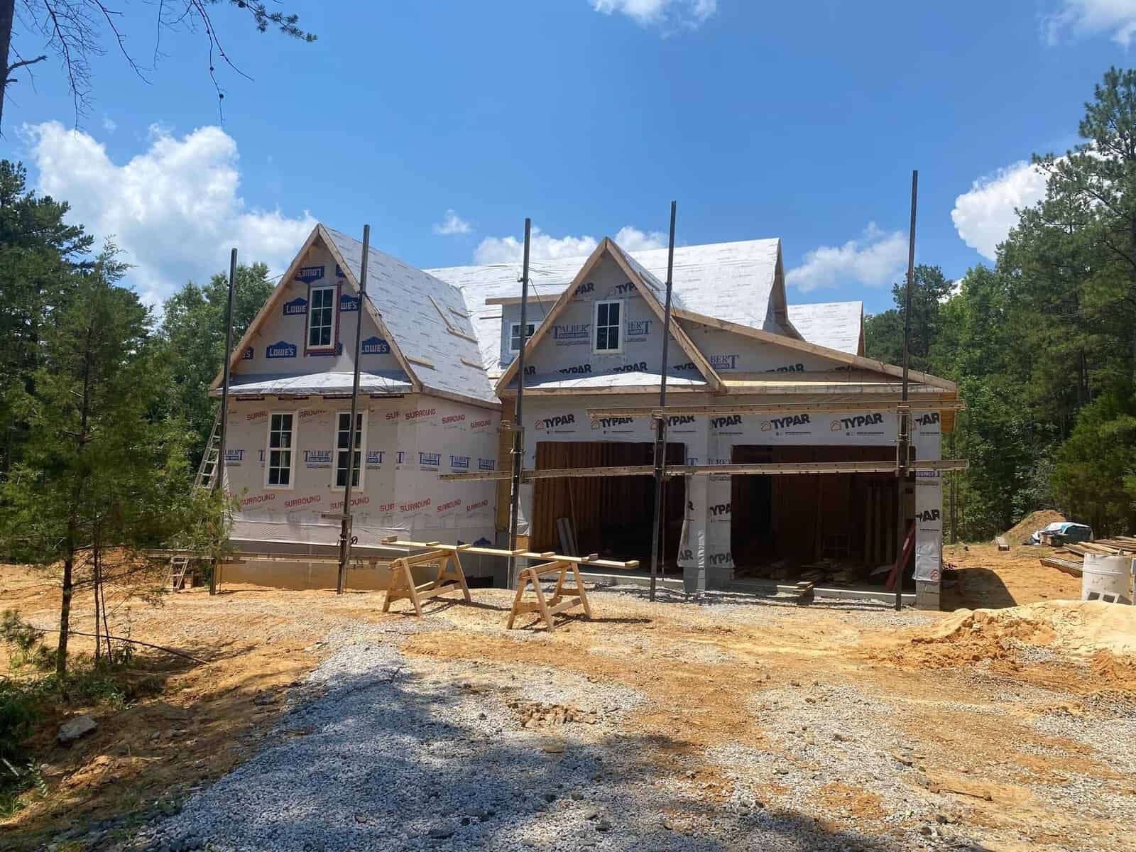 New residential construction site with partially completed houses featuring exposed wooden structures and protective sheathing under a clear sky.