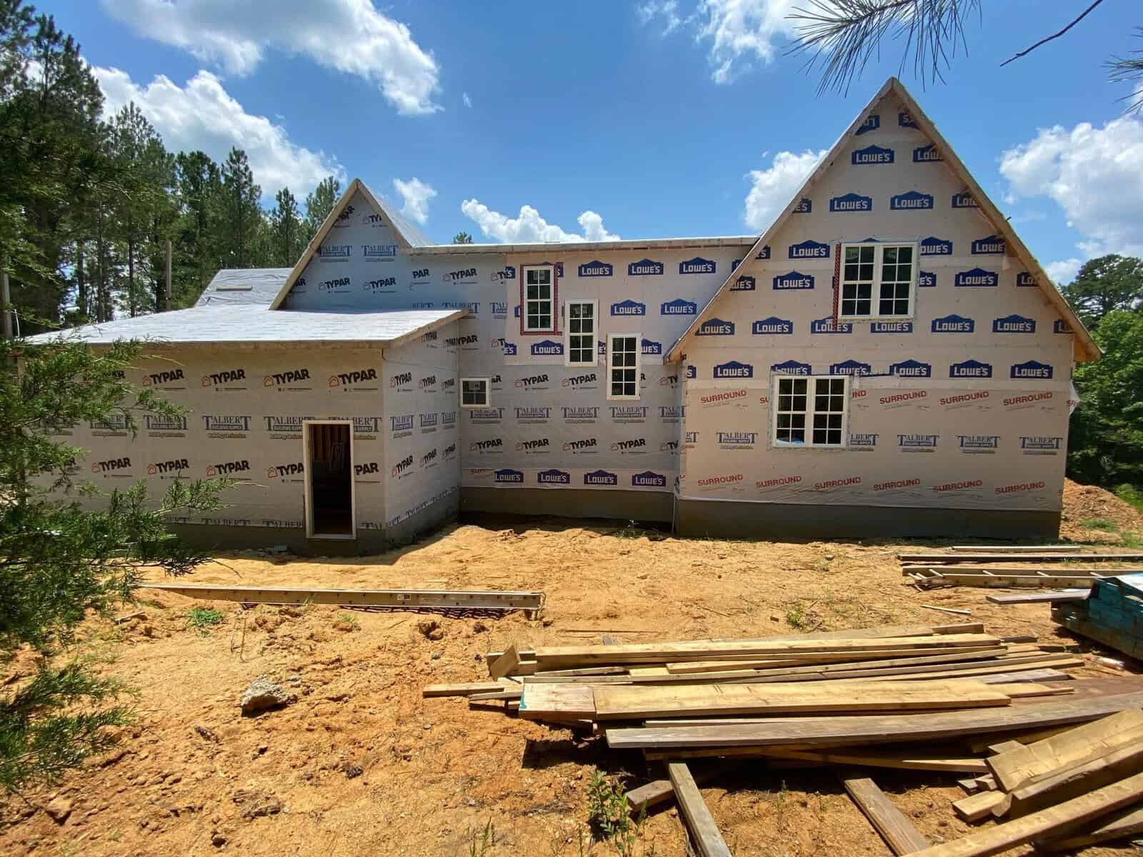 New residential house under construction with exposed insulation wrap and construction materials in the foreground.
