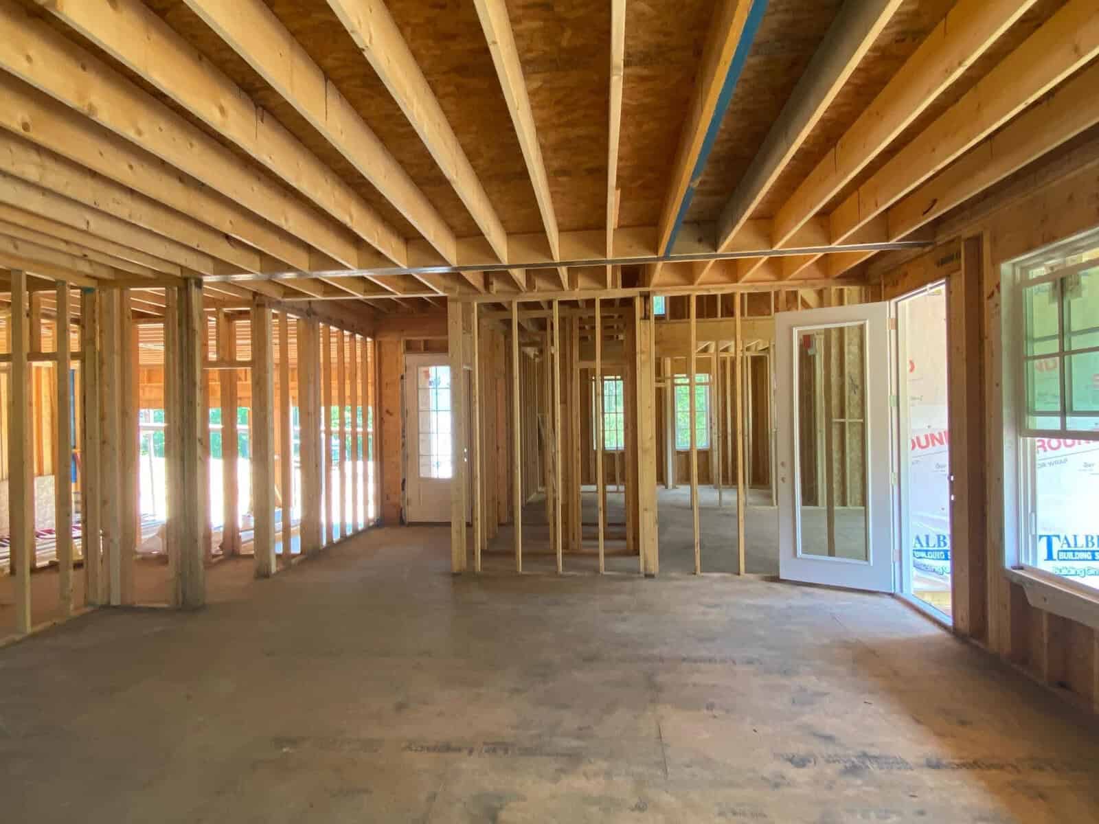 Interior of a residential construction site, showing wooden framing and exposed beams under daylight.