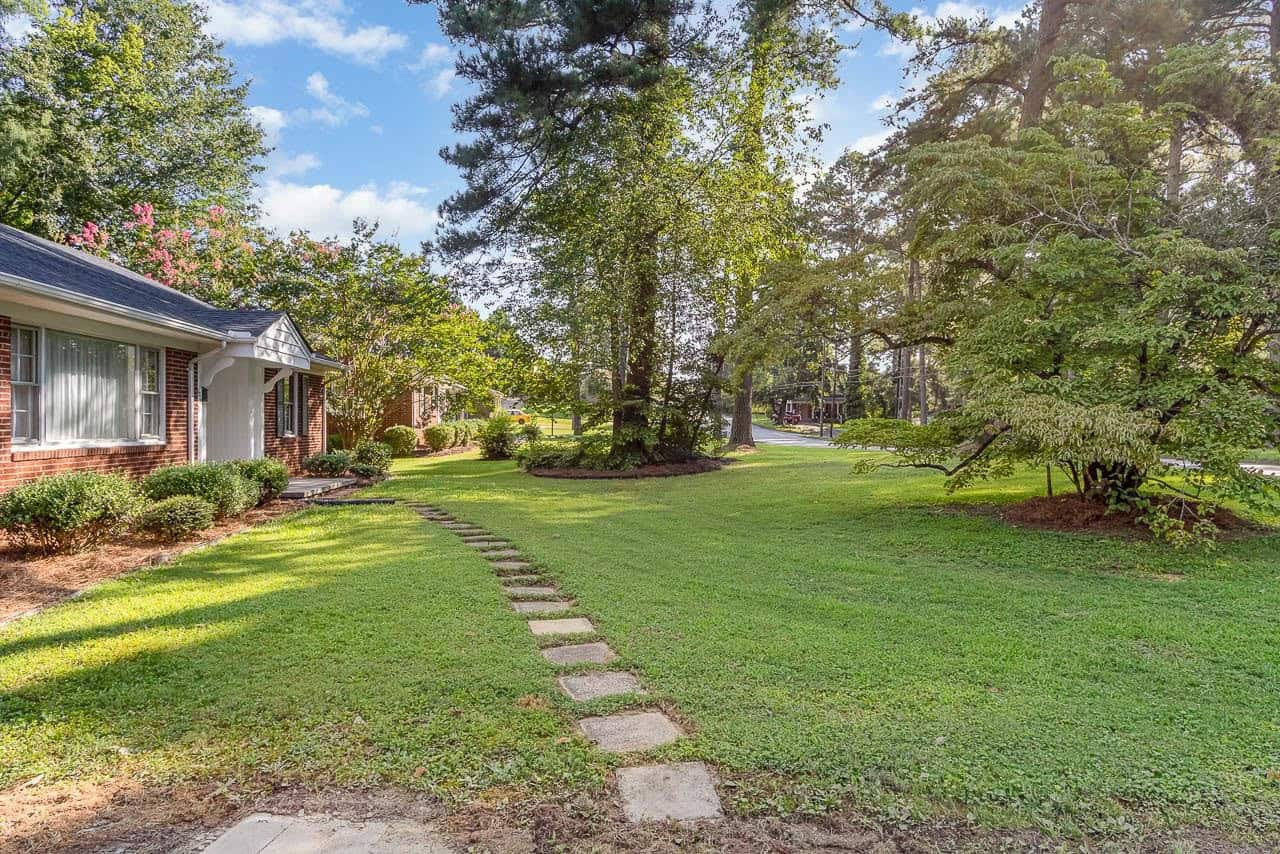A well-manicured lawn in front of a single-story house with a stone pathway and surrounding trees on a sunny day.