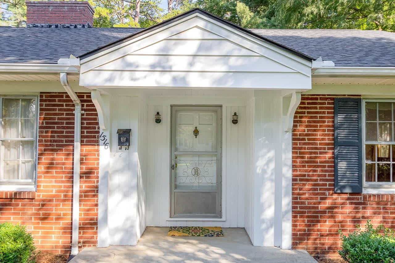 A small, traditional house entrance with a white door, white portico, and red brick walls, displaying the street number 565 on the side.