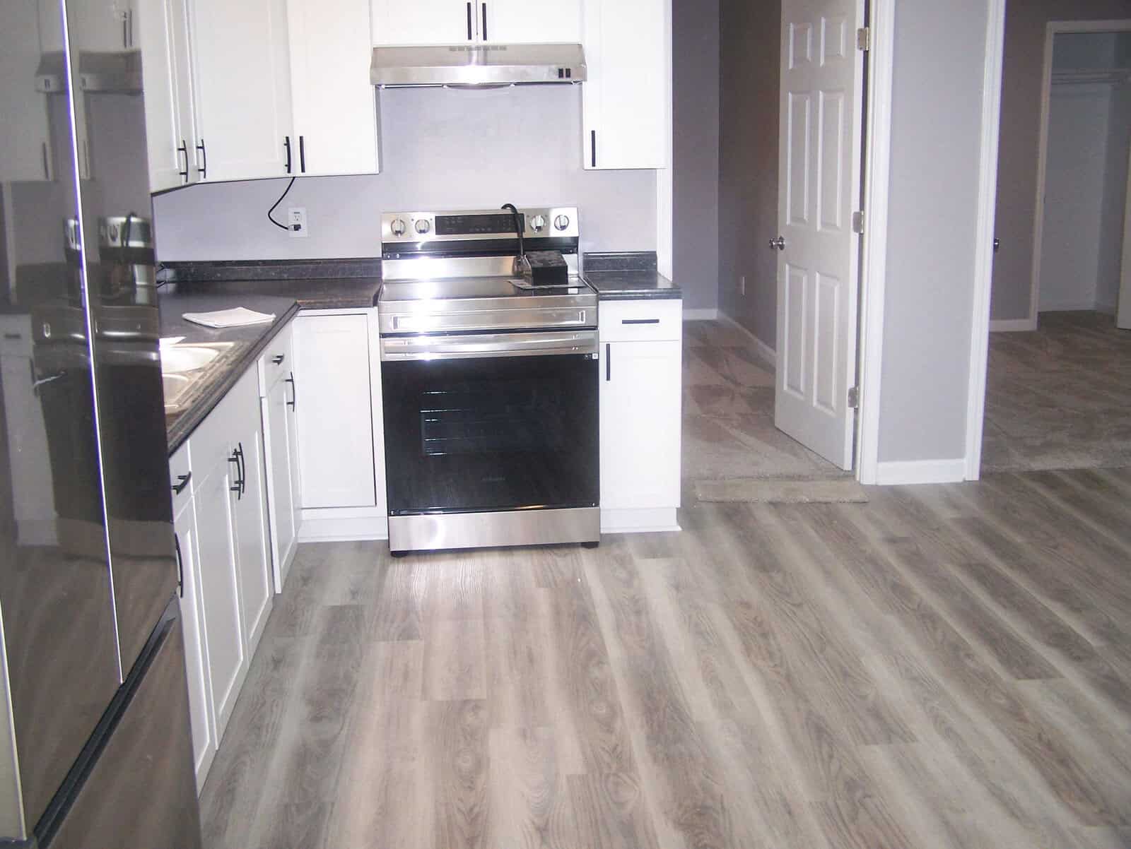 A modern kitchen with stainless steel appliances, white cabinets, and grey laminate flooring.