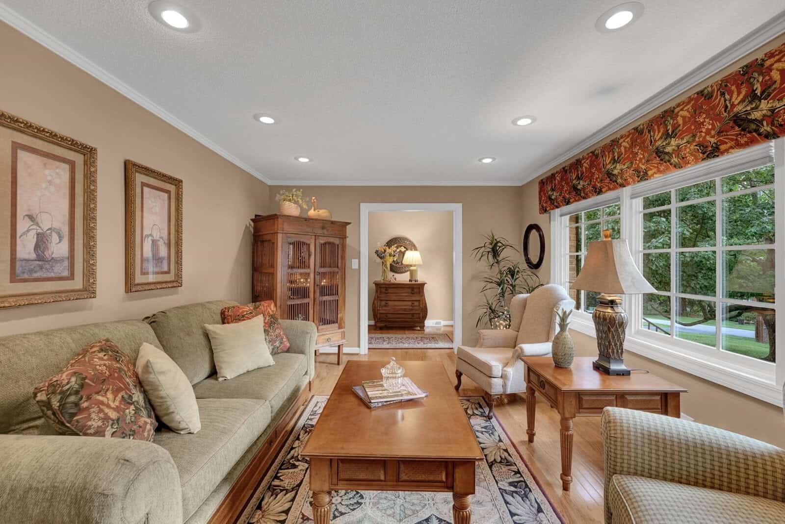 A well-lit, tidy living room with two sofas, a coffee table, and various decorative items, featuring a large window with a garden view at 2106 N Woodland Road.