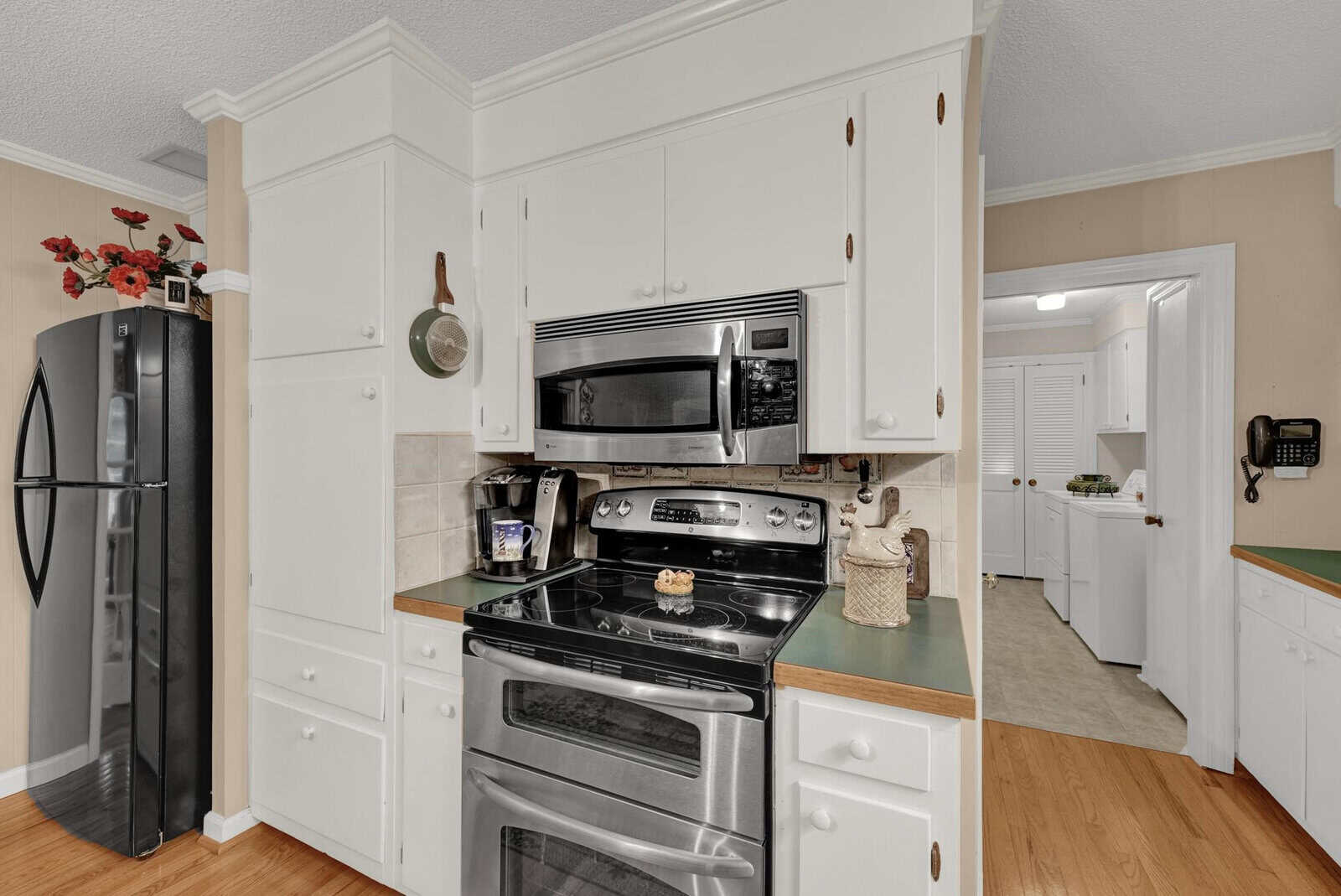 A modern kitchen with white cabinetry, stainless steel appliances, and hardwood flooring.