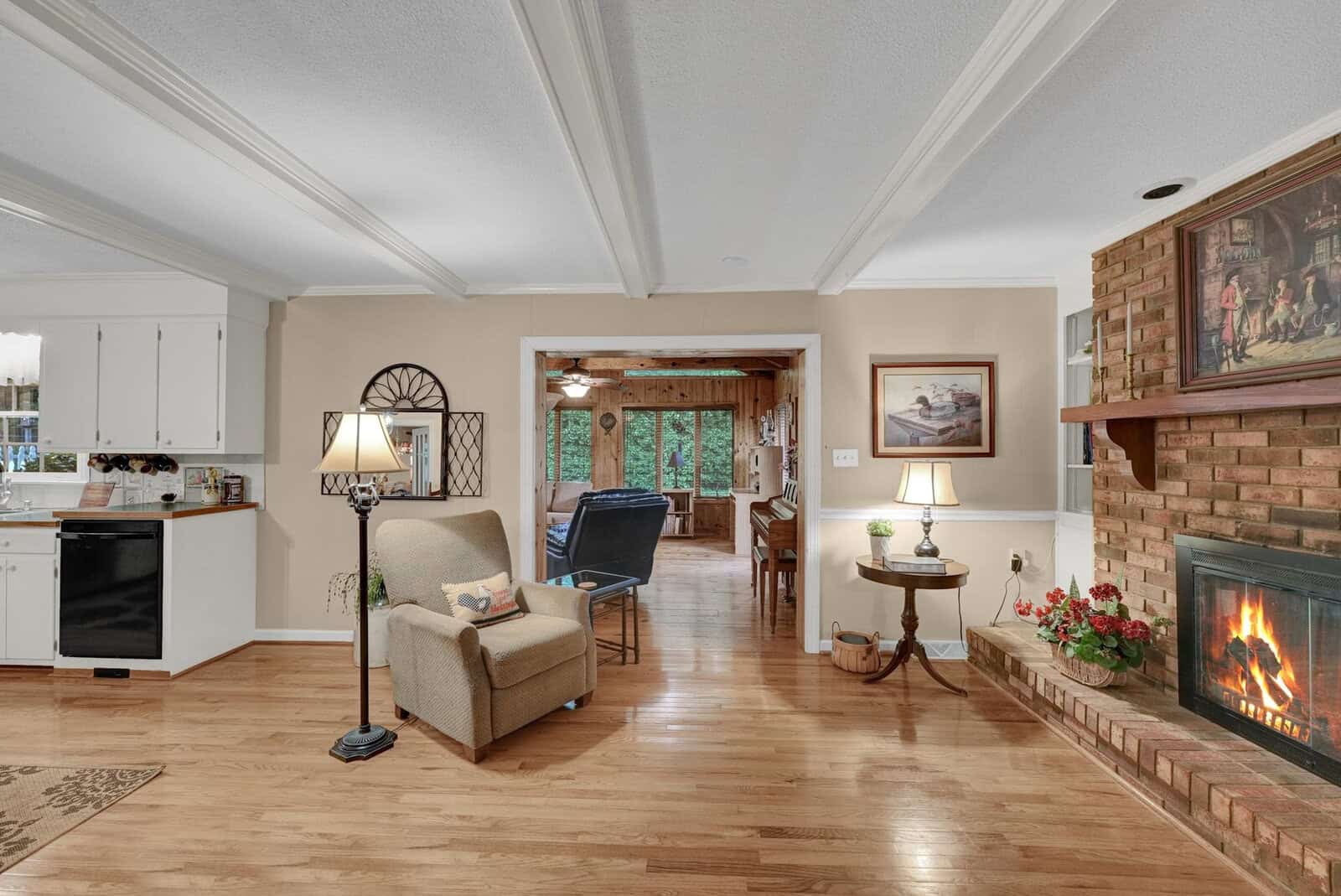 Spacious living room featuring a lit fireplace, hardwood floors, and an open layout leading to an adjacent room with visible kitchen appliances.