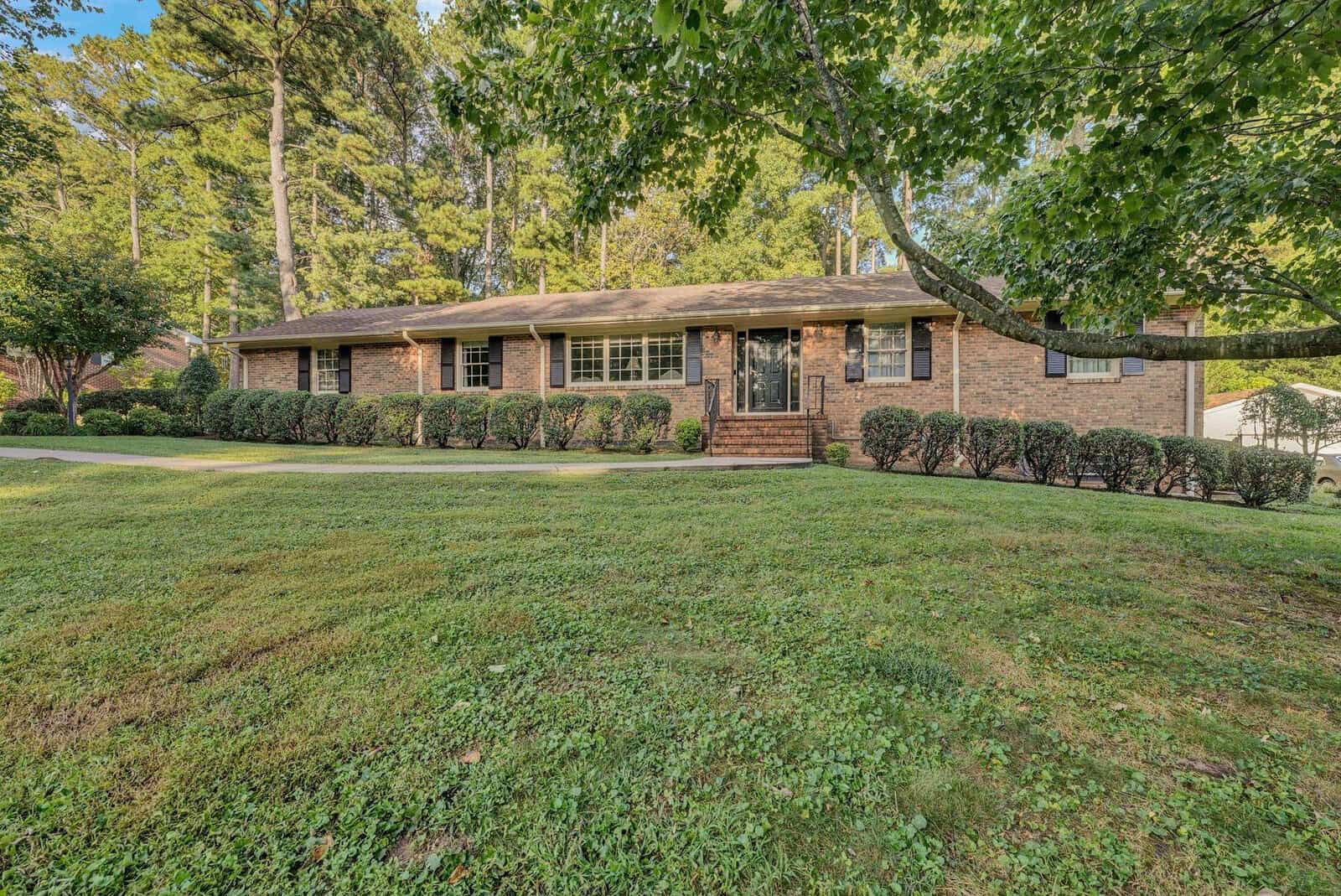Single-story brick house with a large front lawn and surrounding trees.