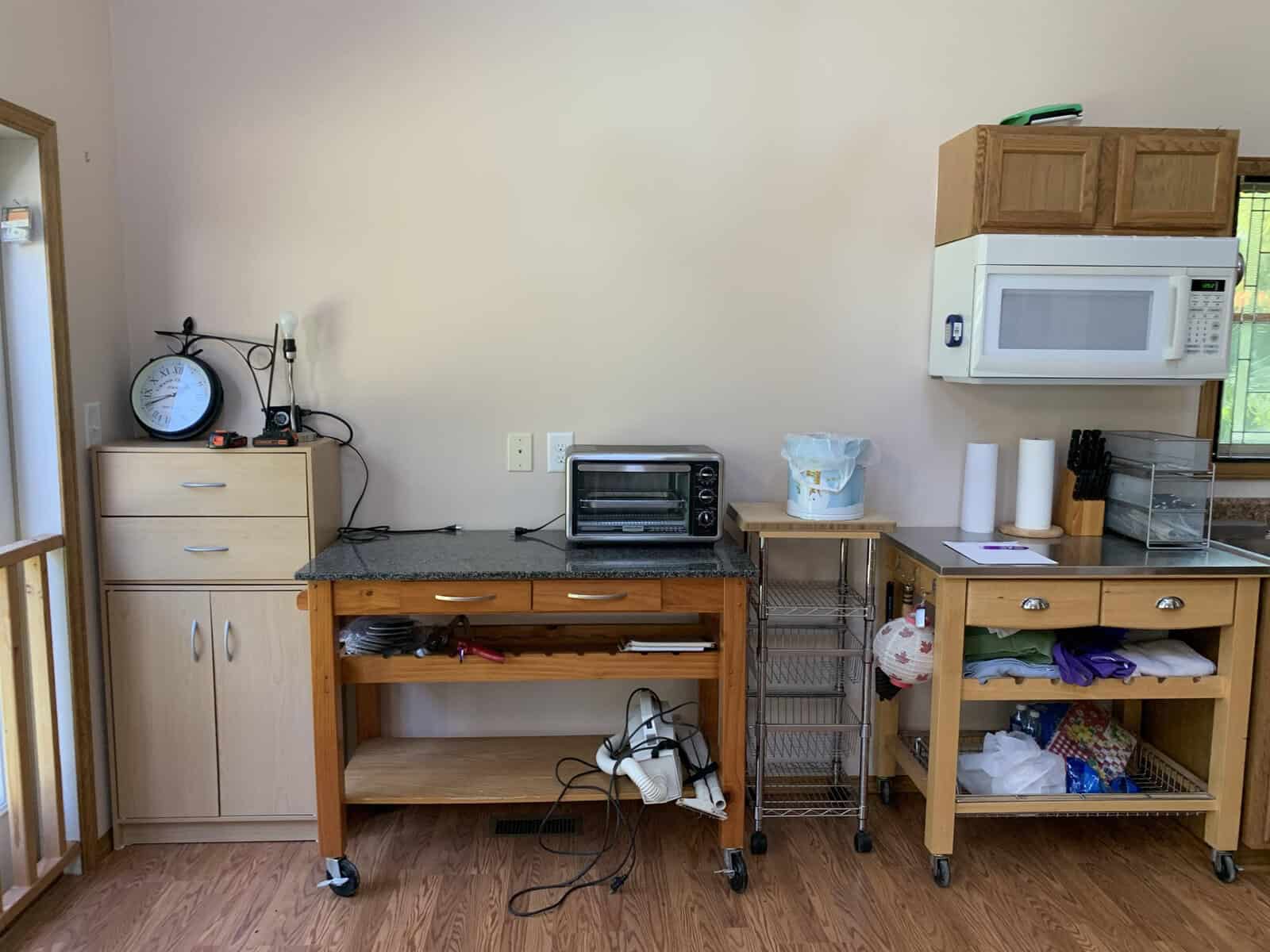 A kitchenette with a microwave, toaster oven, a clock on the countertop, and various storage compartments including a cabinet and drawers with items inside.