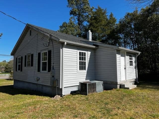 A small, white single-story house with a gabled roof under a clear blue sky.