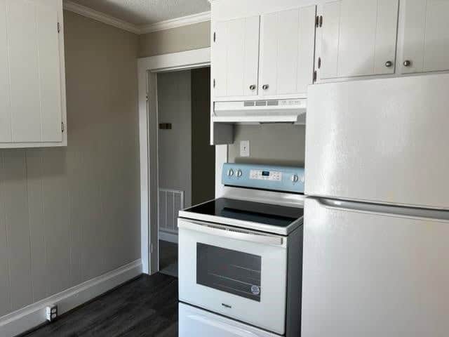 A clean, unoccupied kitchen with white cabinetry, a white electric range oven, and gray walls, appearing to be recently renovated or well-maintained.