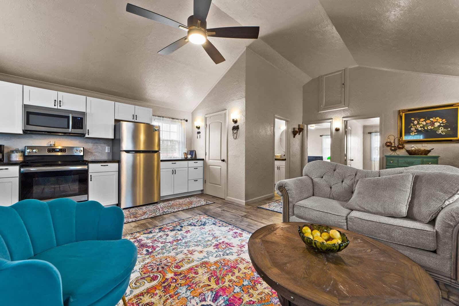 Interior of a modern living room and kitchen with stainless steel appliances, white cabinetry, and colorful area rug.