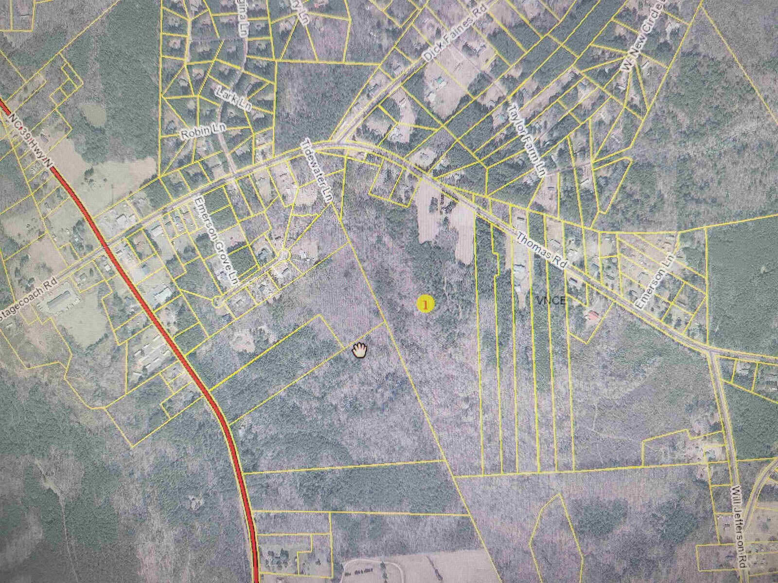 Aerial map view showing a network of streets and land plots with street names labeled and a yellow pin marker indicating a specific location.