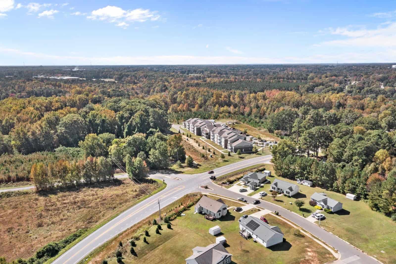 Aerial view of a residential area with mixed housing types, surrounded by trees displaying autumn foliage.