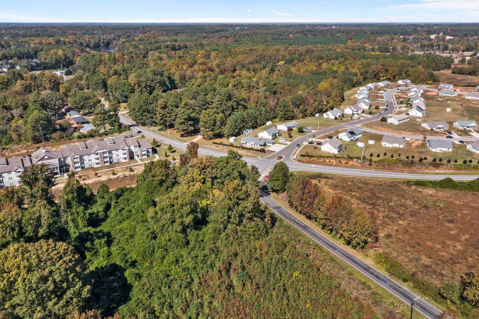 Aerial view of a suburban area showing residential buildings, treelined streets, and surrounding greenery.