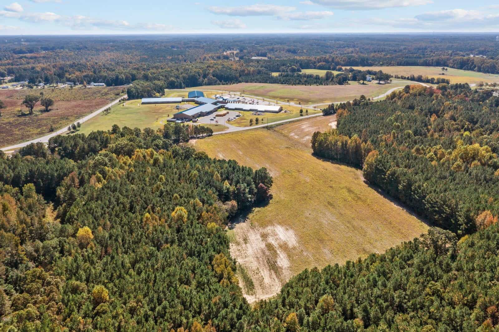 Aerial view of a rural landscape showing a large building complex surrounded by patches of forest and open fields.