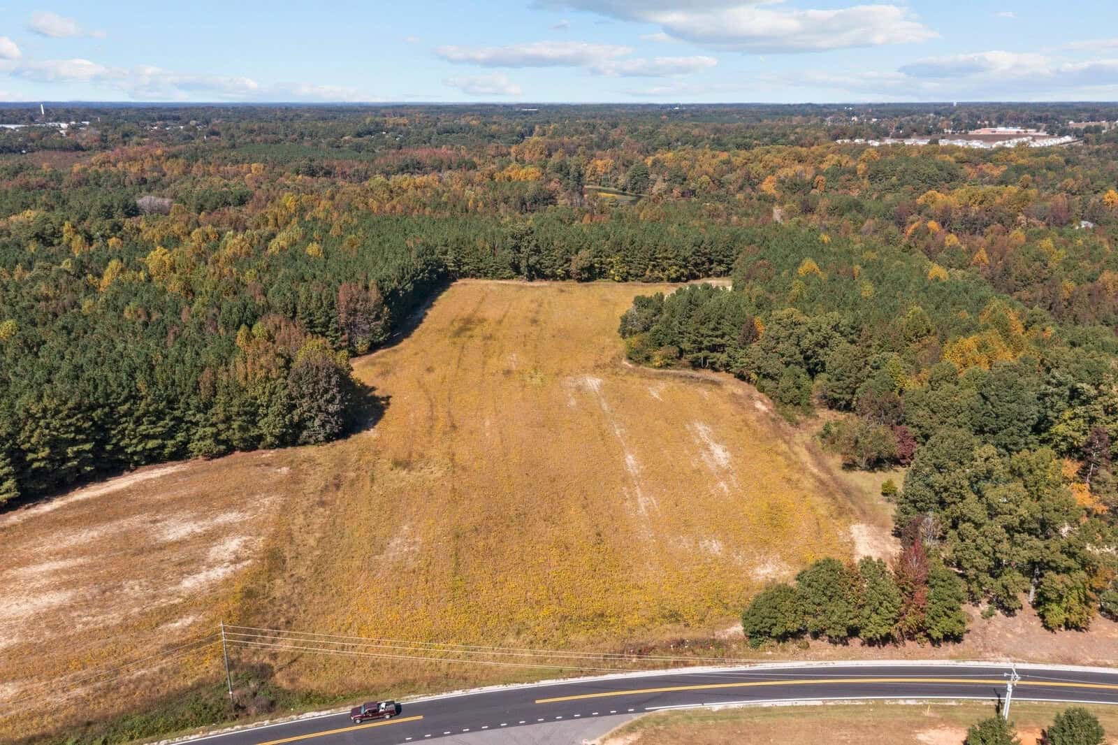 Aerial view of a partially forested landscape with a clearing near a curving road on a sunny day.