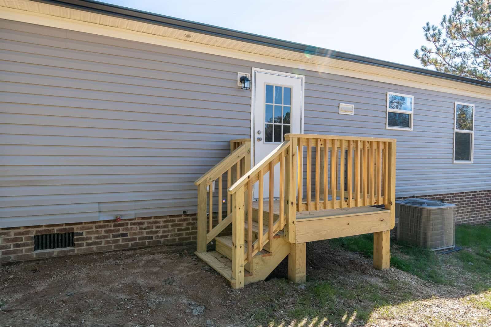 A small wooden deck with steps leads to a back door of a single-story house with vinyl siding, next to an hvac outdoor unit.