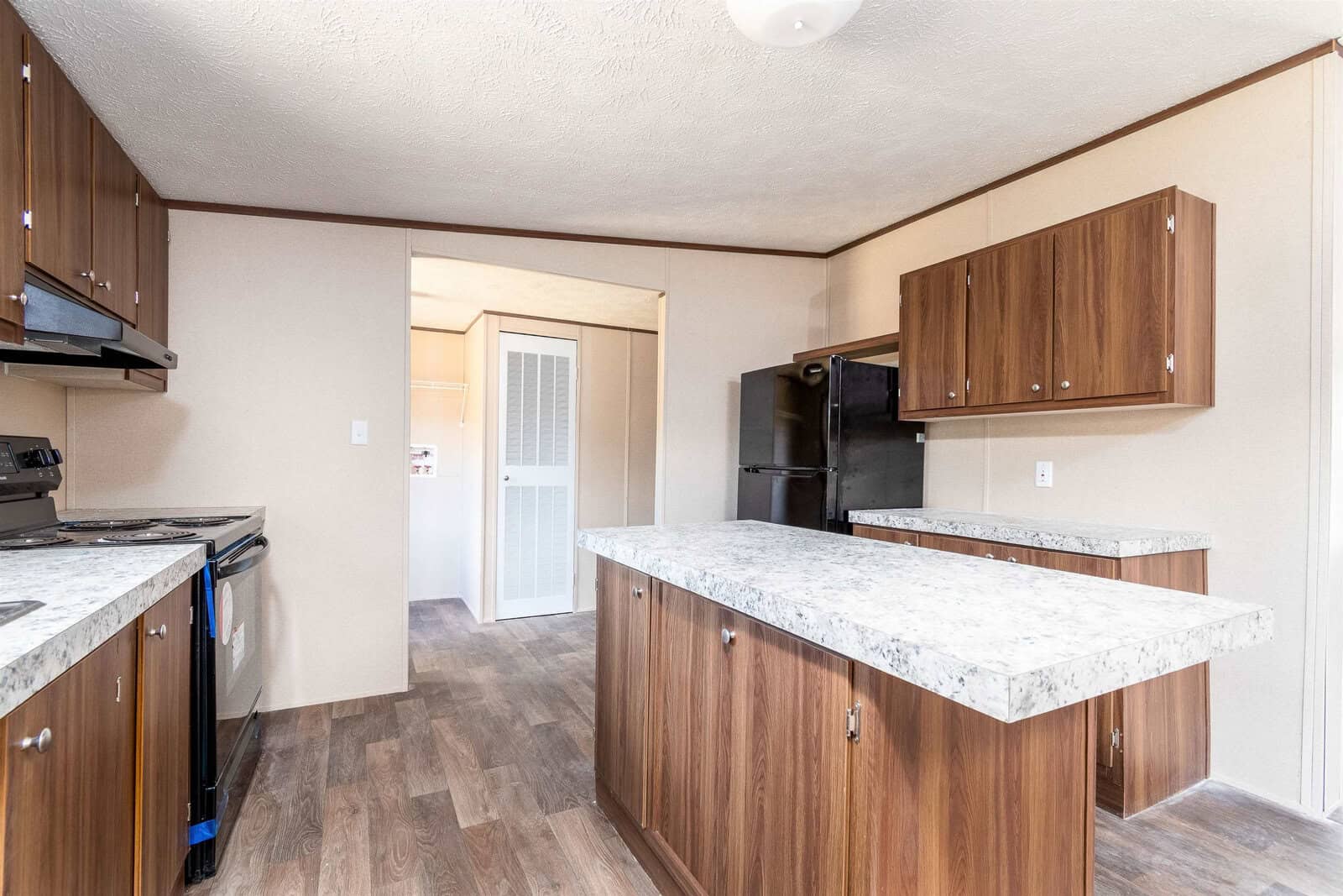A modern kitchen with wooden cabinetry, granite countertops, and stainless-steel appliances, featuring a laminate wood flooring.