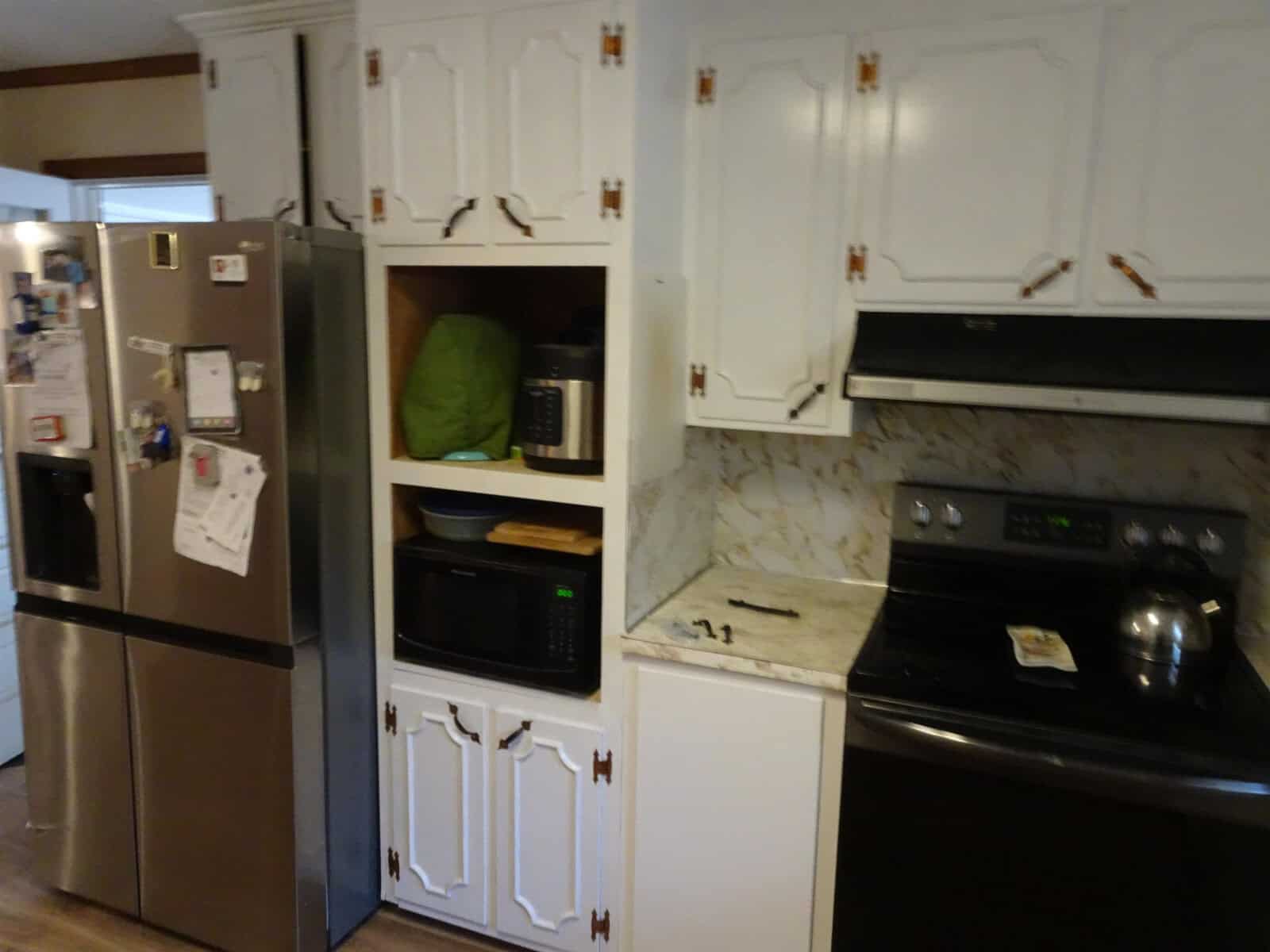 A domestic kitchen featuring stainless steel appliances, white cabinetry, and a countertop with a microwave and various items scattered around.