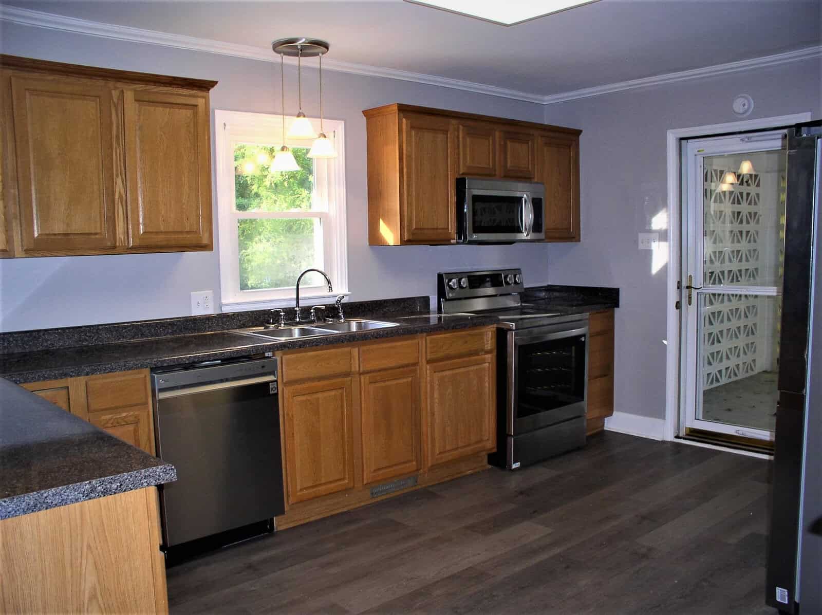 A modern kitchen featuring wooden cabinets, granite countertops, stainless steel appliances, and vinyl flooring.