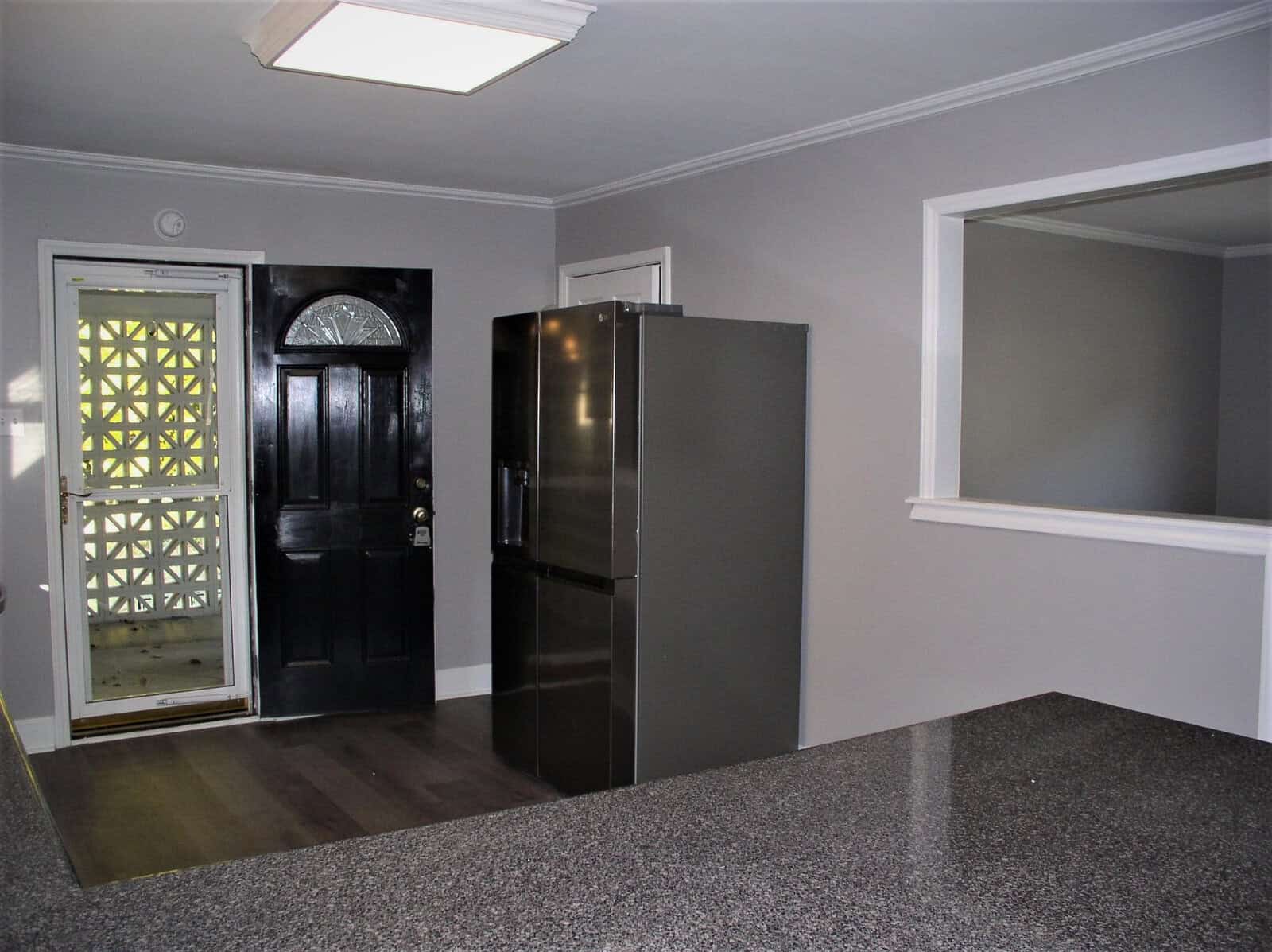 A modern kitchen interior with a stainless steel refrigerator, dark wooden door with glass panels, and gray walls.
