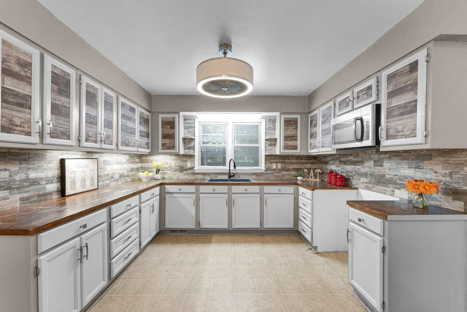 A modern kitchen with white cabinetry, stainless steel appliances, and a stone backsplash with hardwood countertops. there is a window above the sink allowing natural light to illuminate the space.