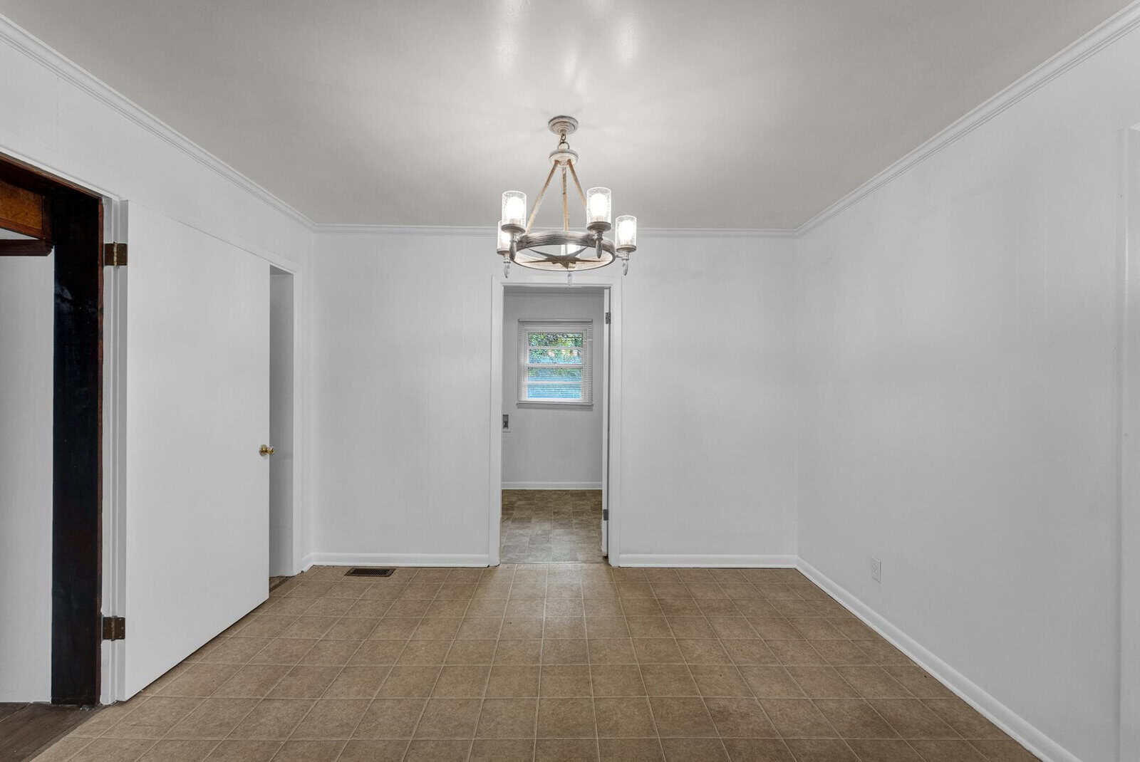 An empty room with white walls, tiled flooring, and a single window at the far end, featuring a central light fixture on the ceiling.
