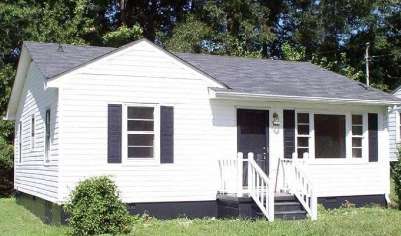A small white single-story house with black shutters, a front porch with steps and a black door.
