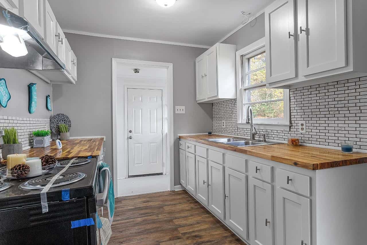 A modern kitchen with white cabinetry, stainless steel appliances, a subway tile backsplash, and wooden countertops, complemented by gray walls and hardwood flooring.