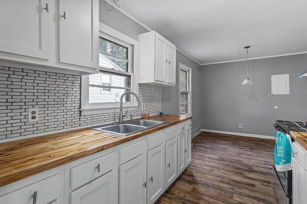A modern kitchen with white cabinetry, stainless steel sink, wooden countertops, and gray walls complemented by a white subway tile backsplash.