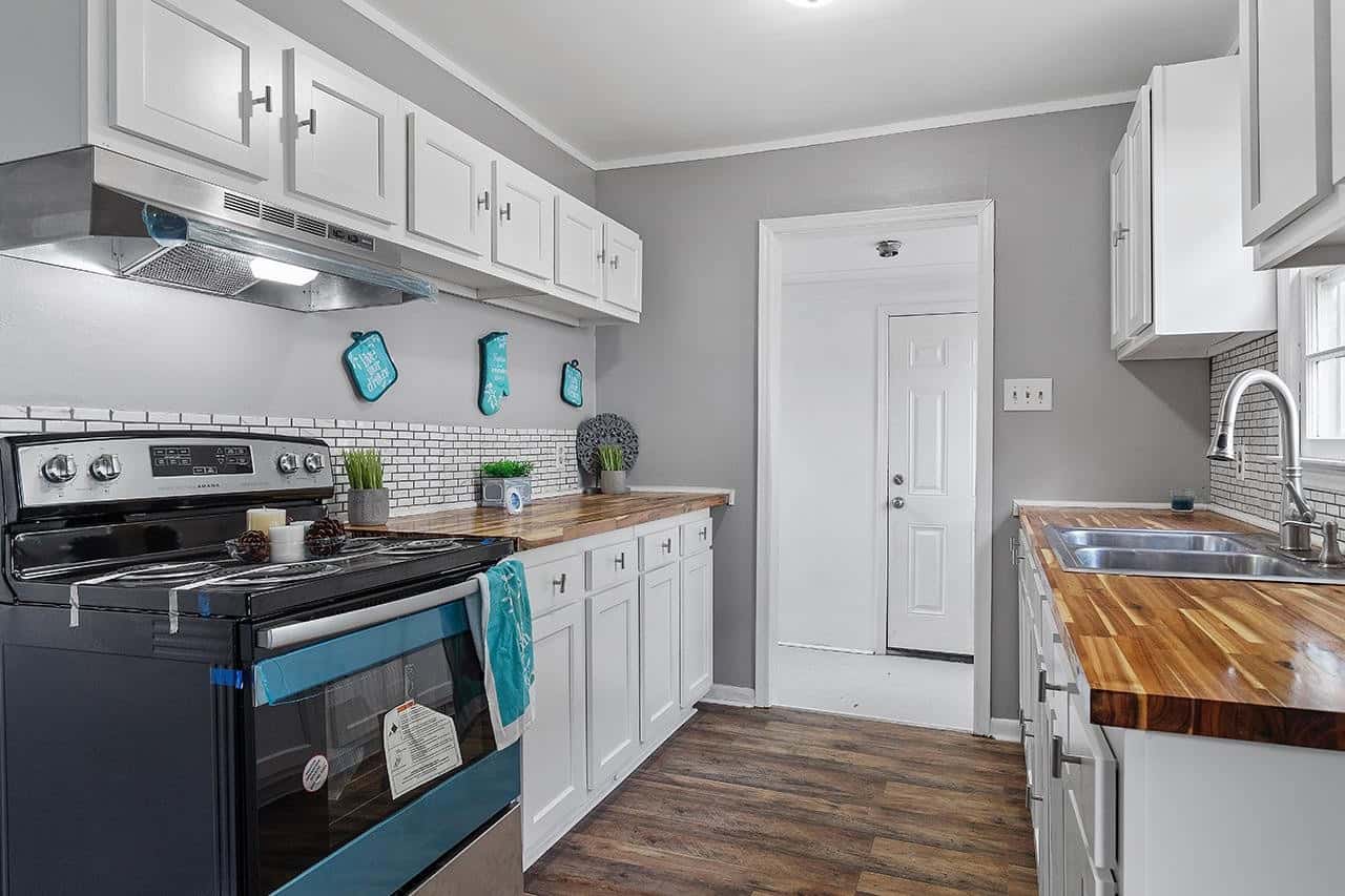 A modern kitchen with white cabinetry, stainless steel appliances, dark hardwood floors, and a wooden countertop.