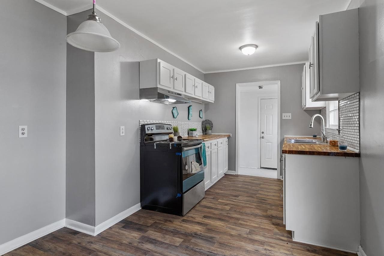 A modern, compact kitchen with white cabinetry, stainless steel appliances, wood countertops, and hardwood flooring.
