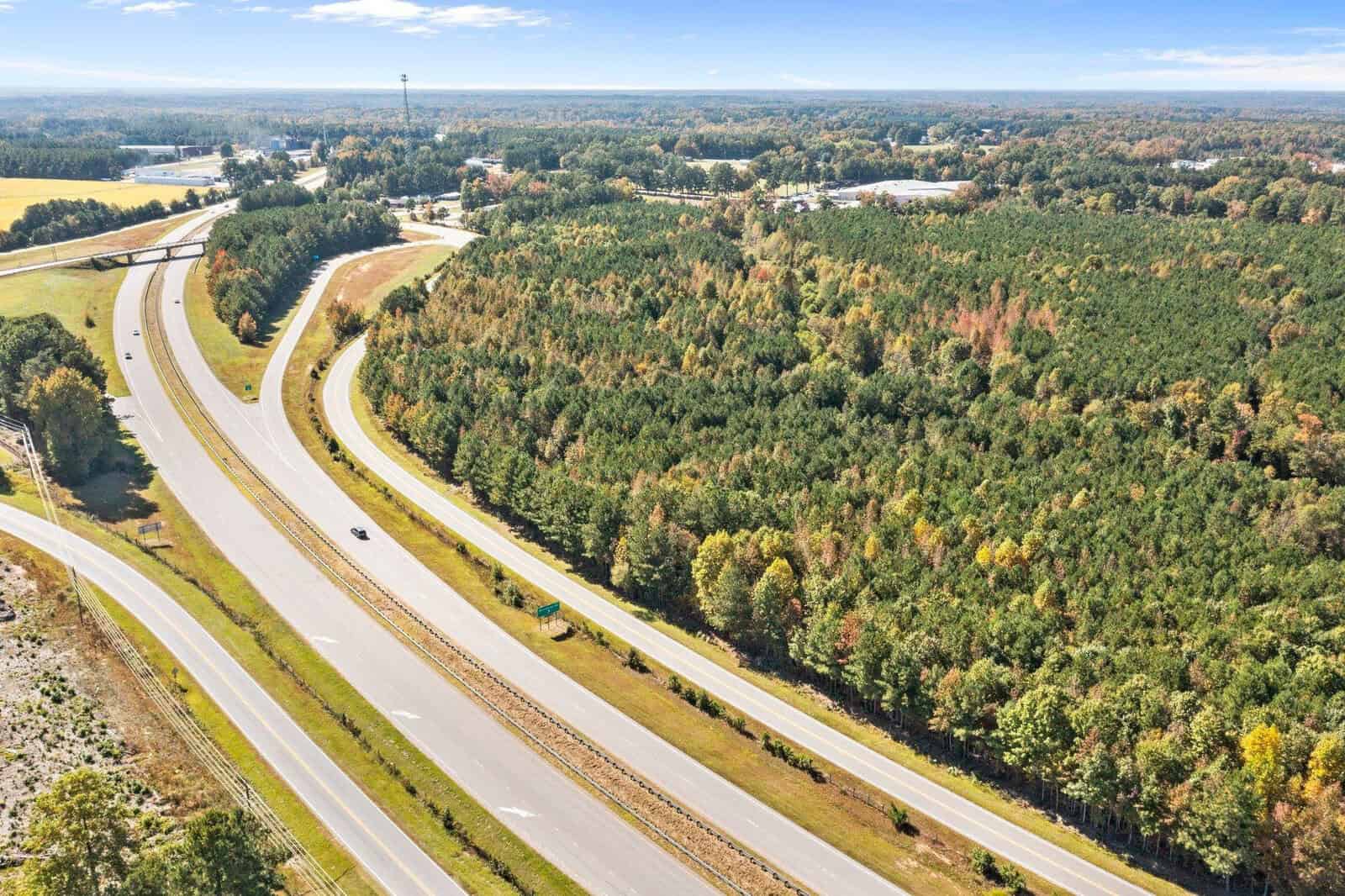 Aerial view of a highway interchange surrounded by woodland with minimal vehicular traffic under clear skies.