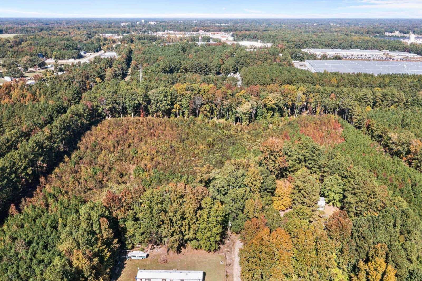 An aerial view of a forested area with autumn foliage, surrounded by roads and urban infrastructure.
