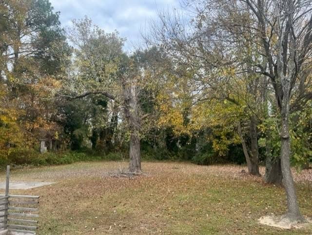 A peaceful, overcast day in a tranquil outdoor setting with leaf-strewn grass, deciduous trees in the midst of losing their foliage, and a glimpse of a structure obscured by vegetation in the background.